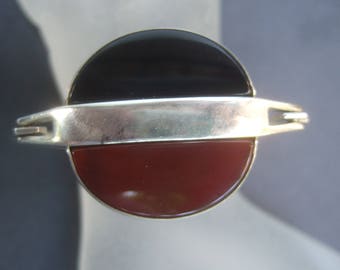 Könnte beinhalten: Ein silberner Ring mit einem schwarzen und roten Stein. Der Ring besteht aus zwei Hälften, die durch ein silbernes Band verbunden sind.