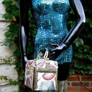K&ouml;nnte beinhalten: Ein blaues Mosaikkleid mit einer gold-wei&szlig; gemusterten Box-Handtasche. Die Handtasche hat einen Klappdeckel und einen Messingverschluss.