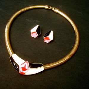 May include: A gold chain necklace with a black, white, and red geometric pendant. The necklace comes with a pair of matching earrings.