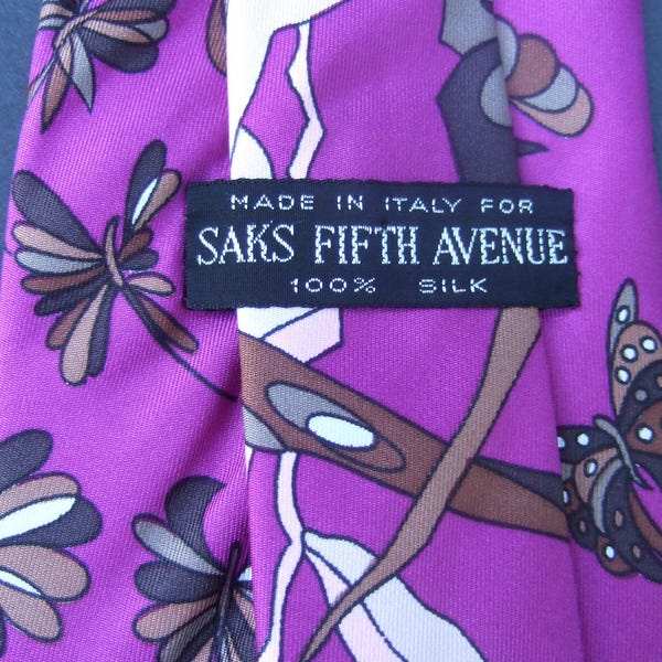 May include: A vibrant purple silk tie with a repeating floral and abstract pattern in shades of brown, white, and gray. The label reads "Made in Italy for Saks Fifth Avenue 100% Silk."