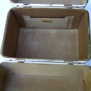 K&ouml;nnte beinhalten: Eine leere, rechteckige Box mit drei F&auml;chern, die mit braunem Stoff ausgekleidet ist, silberfarbene Verzierungen hat und ein kleines Fach im Inneren des oberen Fachs.