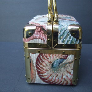 K&ouml;nnte beinhalten: Eine vintage, goldfarbene, rechteckige Handtasche mit einem Tapisserie-Stoffbezug, der ein Muschelmotiv in Rosa-, Blau- und Gr&uuml;nt&ouml;nen zeigt. Die Tasche hat einen oberen Griff und einen Verschluss aus Messing.