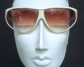 May include: White plastic framed sunglasses with brown gradient lenses. The sunglasses are on a white mannequin head.