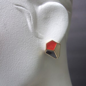 May include: Gold geometric earrings with red, black, and white enamel.