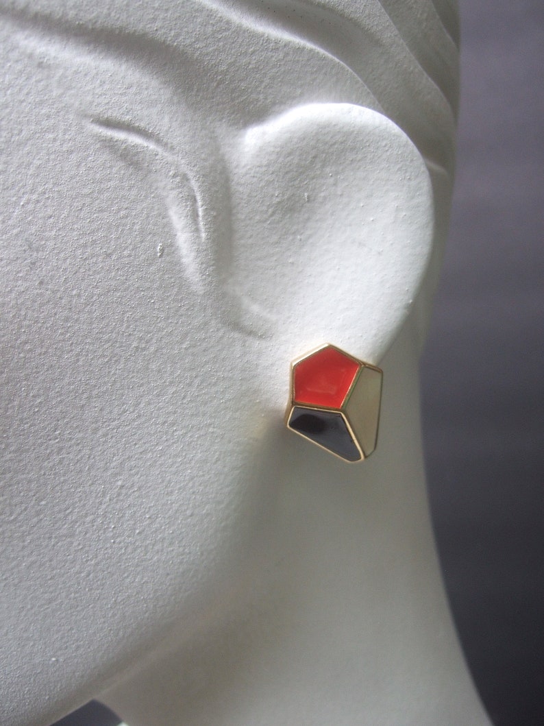 May include: Gold geometric earrings with red, black, and white enamel.