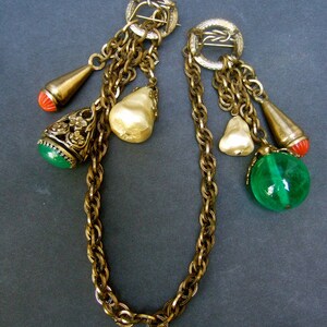 May include: A pair of gold tone chain necklaces with multiple charms, including pearlescent beads, green and red glass beads, and a gold tone pendant with floral details.