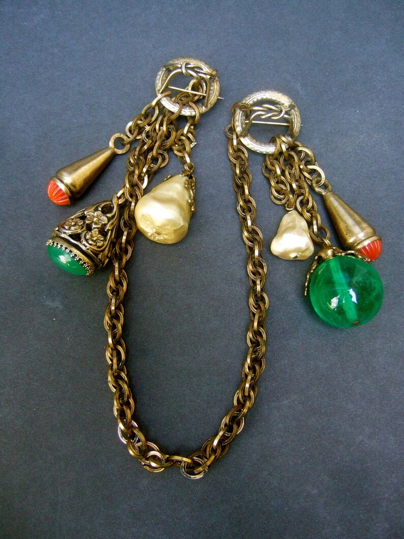 May include: A pair of gold tone chain necklaces with multiple charms, including pearlescent beads, green and red glass beads, and a gold tone pendant with floral details.