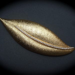 May include: A gold-toned leaf-shaped brooch with a row of clear rhinestones set along the center.