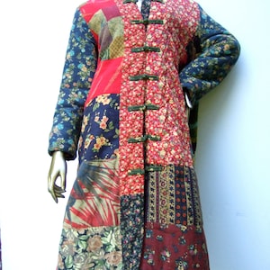 May include: A long, quilted coat with a patchwork design. The coat is made of various floral and geometric fabrics in shades of red, blue, green, and brown. It features a mandarin collar and a row of green buttons down the front.