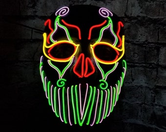 May include: A black neon mask with a skull design. The mask has green, yellow, and red neon lights outlining the skull, eyes, and beard.