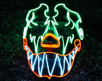 May include: A neon green and orange Halloween mask with a scary, toothy grin. The mask is lit up with LED lights, creating a glowing effect.