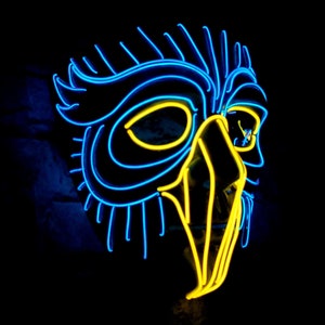 May include: A neon mask in the shape of an owl, with bright blue and yellow lights. The mask has a detailed design with eye and beak features, set against a black background.