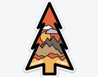 May include: A pine tree-shaped sticker with a sunset scene, mountains, clouds, and a sun. The words "corvallis oregon" are printed on the sticker.