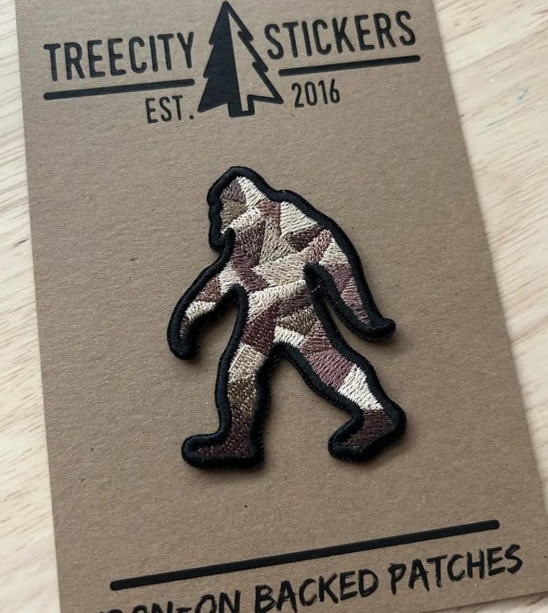 K&ouml;nnte beinhalten: Gestickter Aufn&auml;her mit einem Bigfoot-Design mit schwarzer Umrandung. Der Bigfoot ist mit einem Patchwork aus braunen, beigen und cremefarbenen Farben gef&uuml;llt. Der Aufn&auml;her befindet sich auf einer braunen Karte mit dem Text "TREECITY STICKERS EST. 2016".