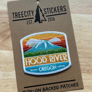 May include: An embroidered patch on a brown card featuring a mountain landscape with a sunset sky, green trees, and the text HOOD RIVER OREGON. The card displays the text TREECITY STICKERS EST. 2016 at the top and IRON-ON BACKED PATCHES at the bottom.