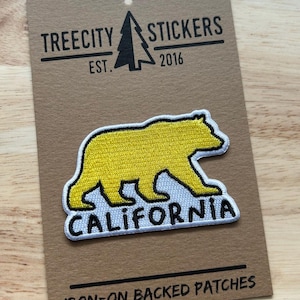 May include: An embroidered iron-on patch featuring a yellow bear silhouette above the black text CALIFORNIA. The patch is mounted on a brown cardboard display card printed with TREECITY STICKERS EST. 2016 and IRON-ON BACKED PATCHES.