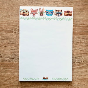 May include: White notepad with a green leafy border and a row of animal faces wearing glasses. The animals include an otter, fox, rabbit, owl, raccoon, and another otter.