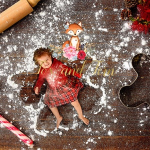 May include: A young child is lying in a pile of white powder, possibly flour, on a wooden surface. The child is wearing a red and black plaid dress and a red shirt. There is a rolling pin, a candy cane, and a gingerbread cookie cutter in the image. The text "Joy and Fern" is written on the surface.