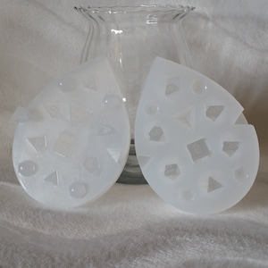 May include: Two white silicone molds with geometric shapes, perfect for making resin crafts. The molds are shaped like teardrops and feature a variety of shapes, including squares, triangles, and circles.