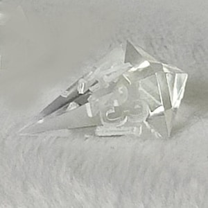 May include: A clear crystal point with a faceted design. The point is sharp and has a reflective surface.