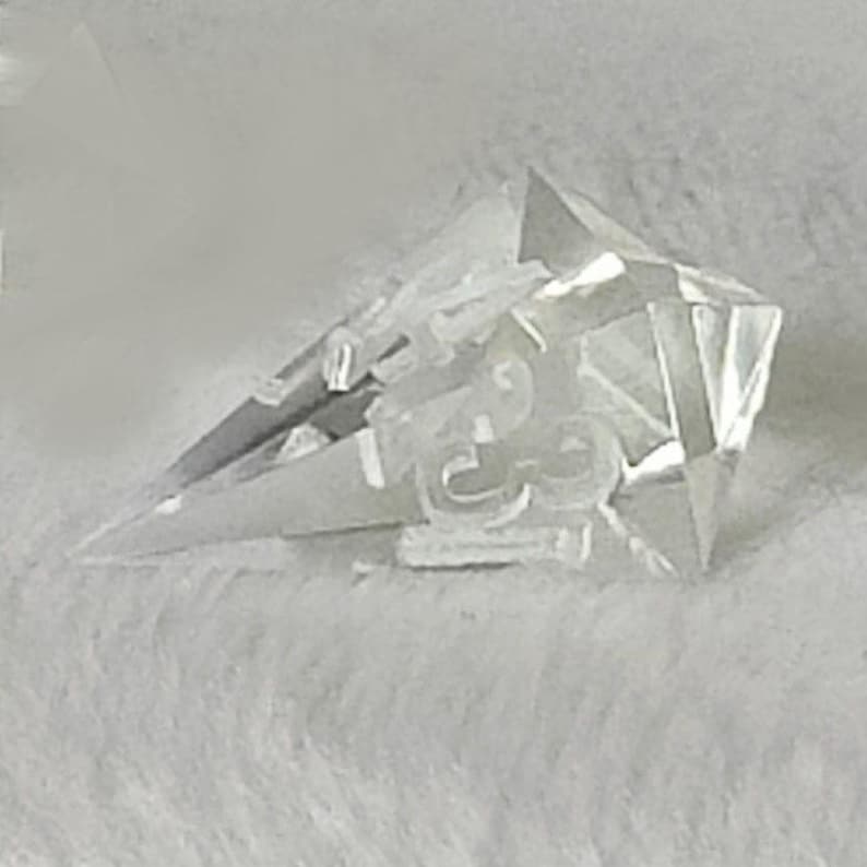 May include: A clear crystal point with a faceted design. The point is sharp and has a reflective surface.