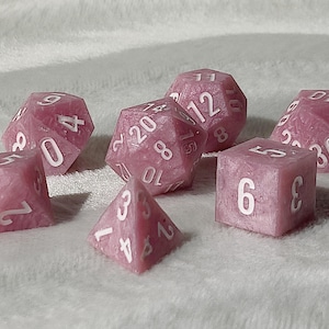 May include: A set of pink dice with white numbers. The dice are in various shapes, including a d4, d6, d8, d10, d12, and d20.