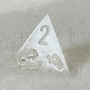 May include: A clear triangular dice with the number 2 on one side and the numbers 3 and 4 on other sides.