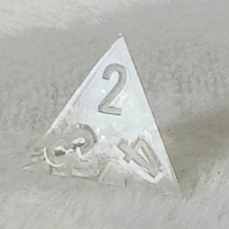 May include: A clear triangular dice with the number 2 on one side and the numbers 3 and 4 on other sides.