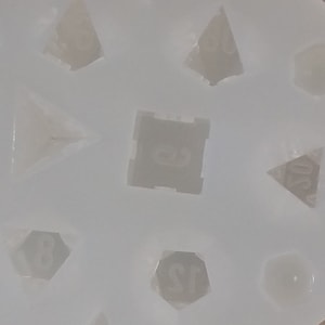 May include: A white silicone mold for making dice. The mold has eight cavities, each shaped like a different type of die. The dice are numbered 4, 6, 8, 10, 12, and 20.