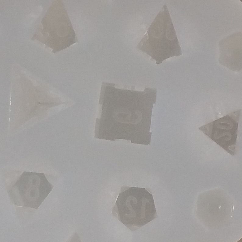 May include: A white silicone mold for making dice. The mold has eight cavities, each shaped like a different type of die. The dice are numbered 4, 6, 8, 10, 12, and 20.