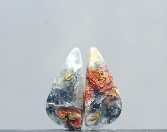 May include: Two teardrop-shaped agate cabochons with a white, gray, and black base. One cabochon has red, orange, and yellow accents. The other cabochon has a more muted color palette with hints of green and blue.