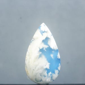 May include: A teardrop-shaped gemstone with a sky-like pattern. The stone features a blue background with white, cloud-like inclusions. The polished surface reflects light, highlighting the natural patterns. This gemstone is suitable for jewelry making.