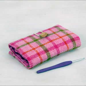 May include: A pink and green plaid fabric needle case with a wooden button closure and a purple crochet hook.