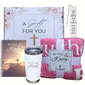 May include: A gift box set with a pink throw blanket, a white tumbler with the text "Be Still & Know PS. 46:10", a journal with the text "Be Still & Know PS. 46:10", and a bookmark with the text "Be Still and Know that I am God Trust in the Lord with all your Heart".