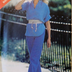 May include: Vintage sewing pattern cover featuring a woman in a blue outfit. The outfit includes a short-sleeved top with a V-neck, matching pants, and a white belt. The pattern is labeled "See & Sew 6945, Size B (14-16-18)".