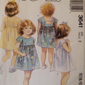 May include: McCall's sewing pattern featuring illustrations of little girls in dresses. The pattern includes designs for dresses with various details, including a striped dress, a dress with a keyhole back, and a dress with a bow.