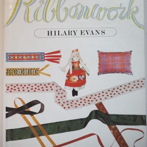 May include: A book titled "Ribbonwork" by Hilary Evans. The cover features a variety of colorful ribbons, including polka dot, striped, and patterned ribbons. There is also a doll wearing a red and white dress and a pillow with a plaid pattern.