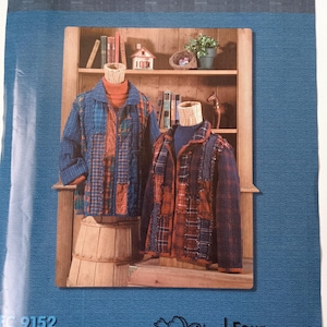 May include: A sewing pattern titled "Raggy Jacket" by Fat Quarters & More. The pattern features two patchwork jackets in blue and rust colors displayed on mannequins. The background includes a wooden shelf with books and decorative items. The pattern is designed by Marjorie Webb & Sandra Noah.