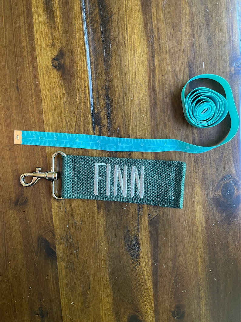 May include: A green fabric keychain with a silver clip and the name "FINN" embroidered in white.