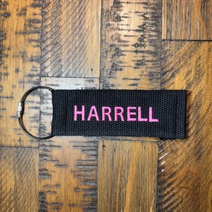 May include: Black key chain with a silver ring and the name "HARRELL" embroidered in pink.