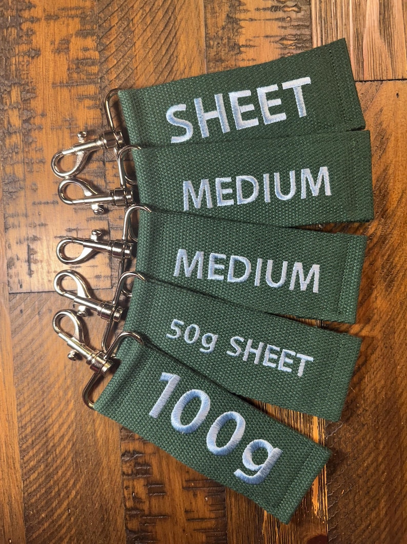 May include: Five green fabric keychains with silver key rings. The keychains are labeled with the text "SHEET", "MEDIUM", "MEDIUM", "50g SHEET", and "100g".