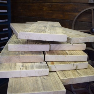 Puede incluir: Una pila de tablones de madera rectangulares de color claro con patrones de veta visibles y textura natural. Las tablas est&aacute;n dispuestas en una pila escalonada, mostrando los bordes crudos y los tonos beige y gris de la superficie.