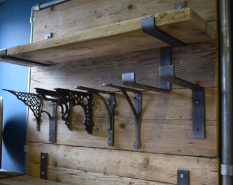Puede incluir: Un expositor de pared con un estante de madera natural sostenido por soportes de metal oscuro. Debajo del estante, una serie de cinco soportes de metal oscuro están fijados al panel de madera vertical, mostrando diversos diseños.