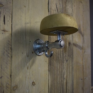 May include: A silver metal coat hook with a wooden hat rack attached to a wooden wall. The hook is in the shape of a pipe with a hook on the end. The hat rack is a round piece of wood.