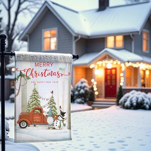 May include: A rectangular Christmas garden flag with a winter scene. The flag features a red truck, Christmas trees, and a snowman. The text "MERRY Christmas AND HAPPY NEW YEAR" is displayed in red script. The flag is displayed in front of a snow-covered house.