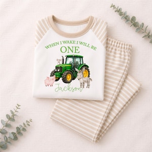 May include: A white long-sleeve shirt with beige striped raglan sleeves and matching striped pants. The shirt features a green tractor graphic, a pig, a donkey, a mouse, and the text "WHEN I WAKE I WILL BE ONE" and the name "Jackson" in green.