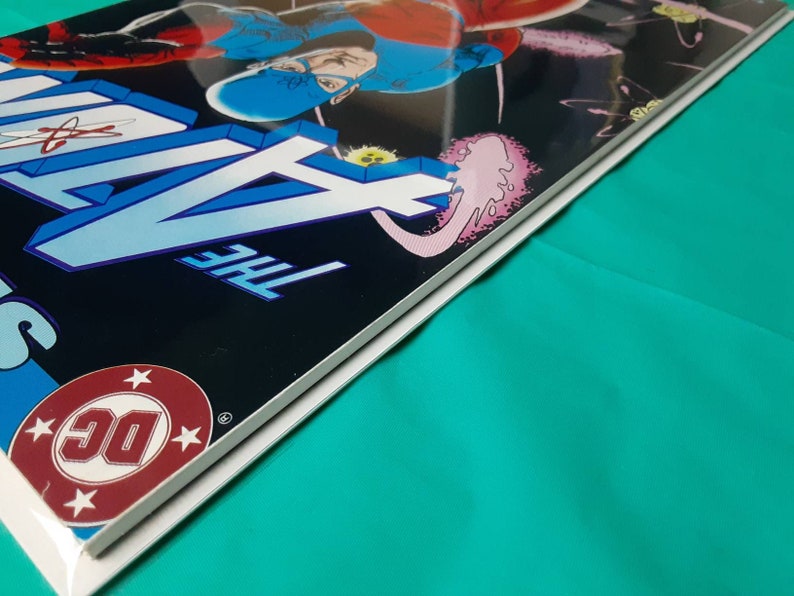 May include: A close-up of the spine of a comic book with a blue and black cover. The title "The New Gods" is printed in white on the cover. The DC Comics logo is visible in the lower left corner.