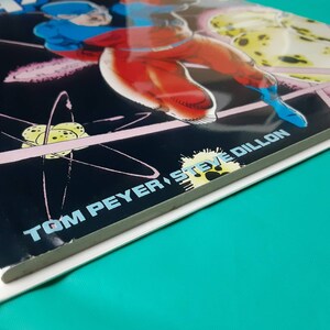 May include: A comic book cover featuring a superhero in a blue and red costume flying through space. The cover is titled "Atom" and features the artist's name "Tom Peyer, Steve Dillon".