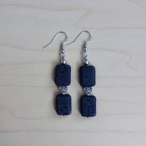 May include: A pair of black lava rock earrings with silver Celtic knot charms. The earrings are dangle style and have a silver hook closure.