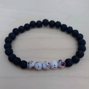 May include: A black lava rock beaded bracelet with white beads accented with red speckles.